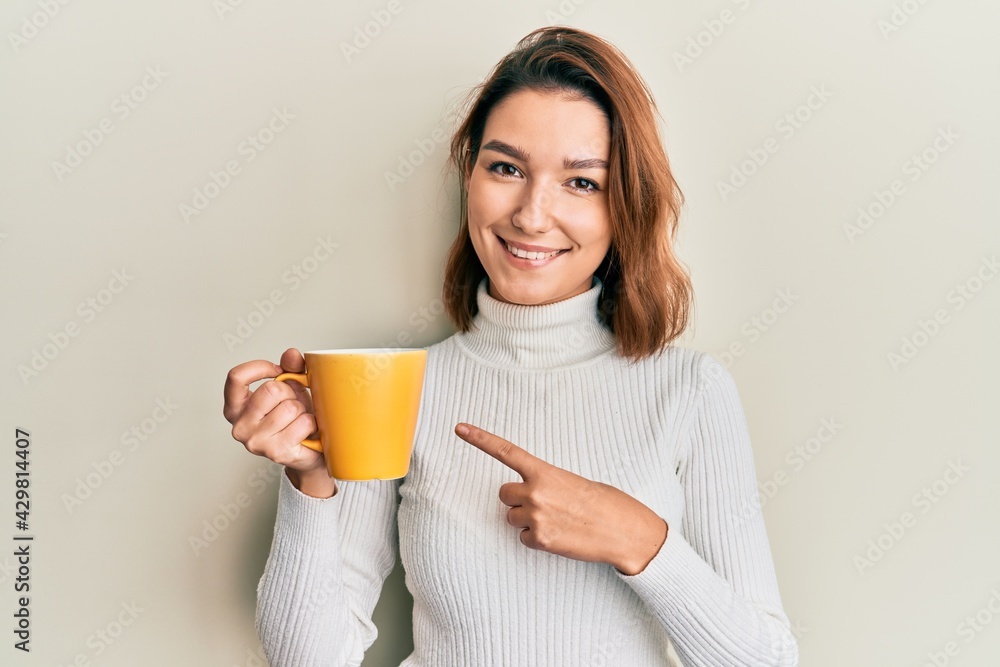 Young caucasian woman holding coffee smiling happy pointing with hand and finger Young caucasian woman holding coffee smiling happy pointing with hand and finger