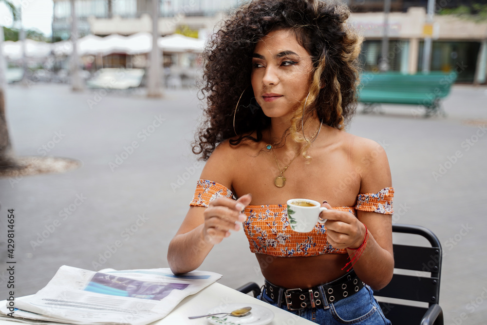 Young afro colombian woman sitting at cafe drinking coffee and reading  newspaper. Stock Photo