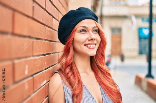 Young redhead girl wearing french style leaning on the wall at the city