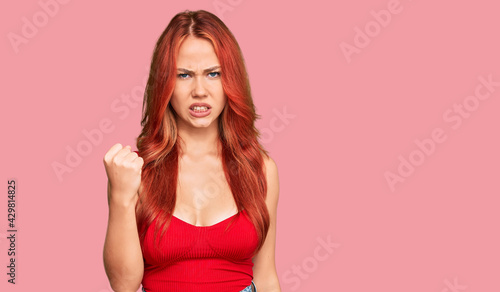 Young redhead woman wearing casual clothes angry and mad raising fist frustrated and furious while shouting with anger. rage and aggressive concept.