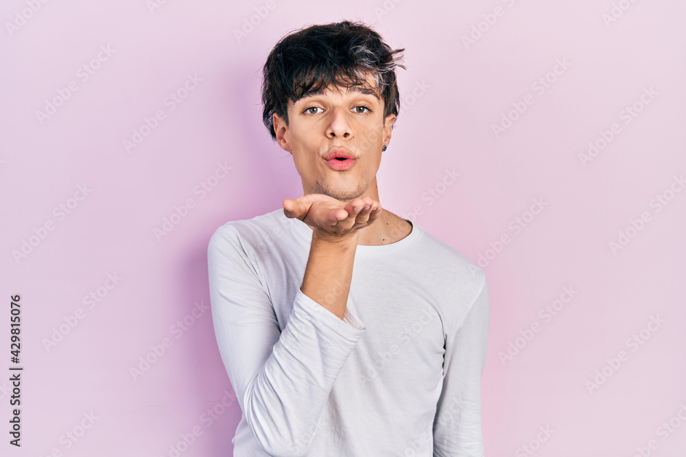 Handsome hipster young man wearing casual white shirt looking at the camera blowing a kiss with hand on air being lovely and sexy. love expression. Handsome hipster young man wearing casual white shirt looking at the camera blowing a kiss with hand on air being lovely and sexy. love expression.