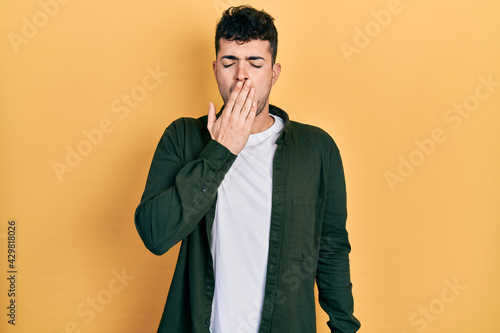 Young hispanic man wearing casual clothes bored yawning tired covering mouth with hand. restless and sleepiness.