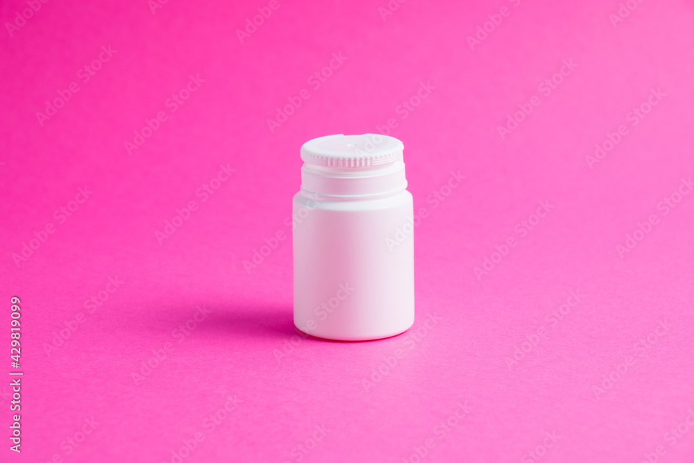 White jar of pills or vitamins on a pink paper background. Medicine on background with copy space. White jar of pills or vitamins on a pink paper background. Medicine on background with copy space.