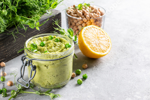 Avocado hummus in a glass jar with chickpeas, green peas, spices on gray background. Healthy vegan dip. copy space.