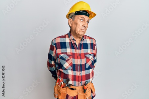 Senior hispanic man wearing handyman uniform smiling looking to the side and staring away thinking.
