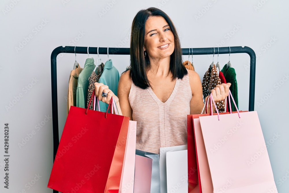 Middle age brunette personal shopper woman holding shopping bags winking  looking at the camera with sexy expression, cheerful and happy face. Stock  Photo | Adobe Stock