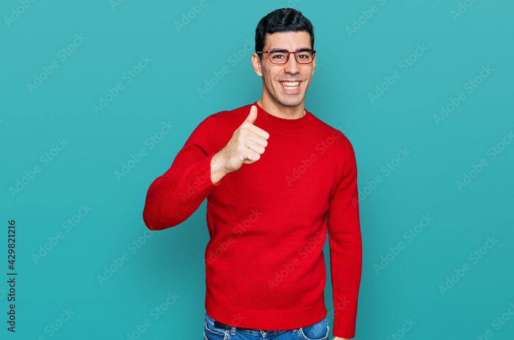 Handsome hispanic man wearing casual clothes and glasses doing happy thumbs up gesture with hand. approving expression looking at the camera showing success. Handsome hispanic man wearing casual clothes and glasses doing happy thumbs up gesture with hand. approving expression looking at the camera showing success.