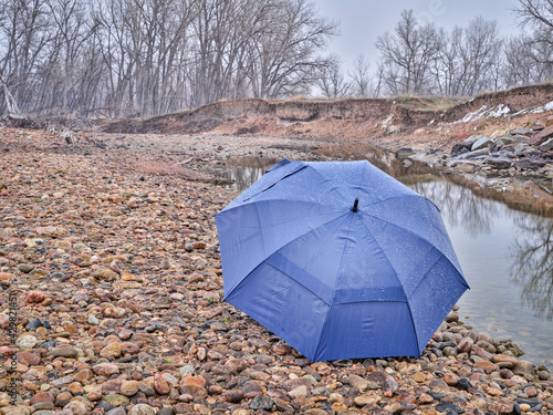 umbrella on a river shore in early spring scenery with a low water and falling snow