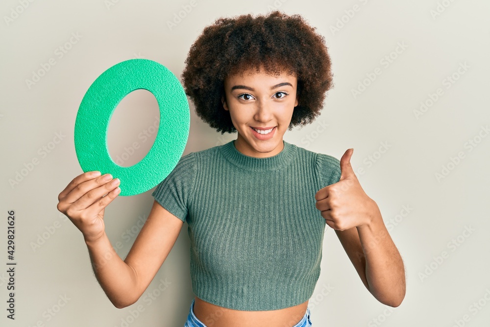 Young hispanic girl holding number zero smiling happy and positive, thumb up doing excellent and approval sign Young hispanic girl holding number zero smiling happy and positive, thumb up doing excellent and approval sign