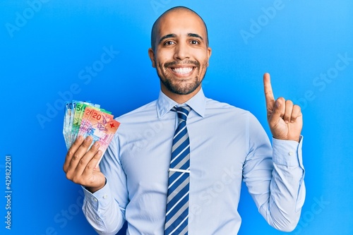 Hispanic adult business man holding swiss franc banknotes smiling with an idea or question pointing finger with happy face, number one