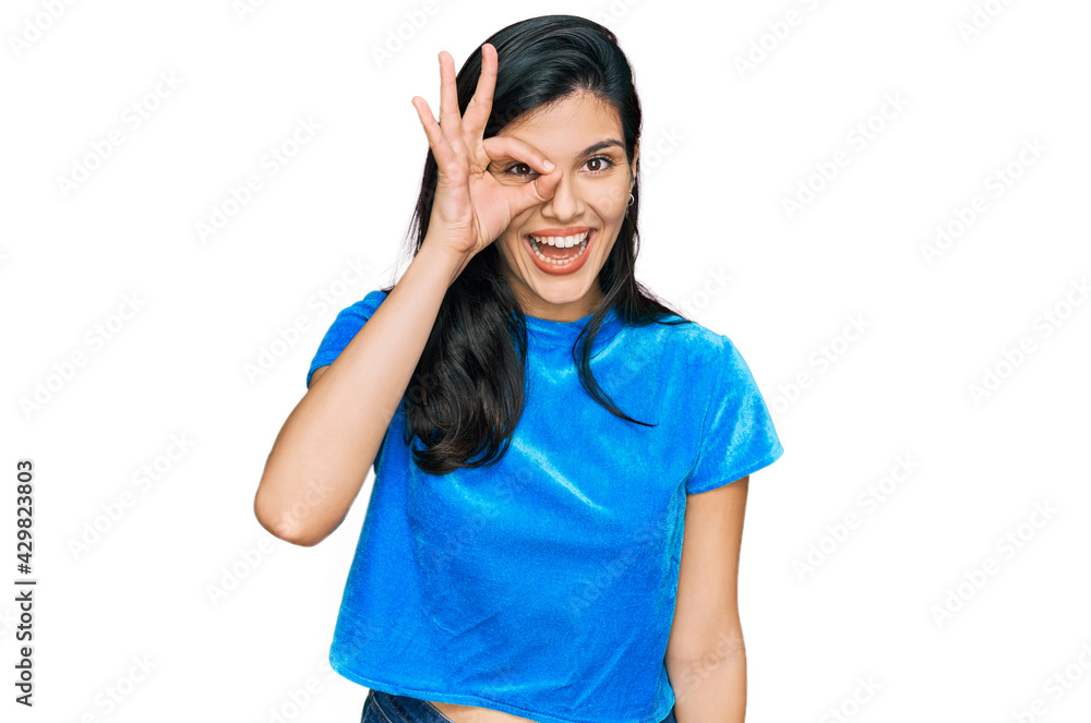 Young hispanic woman wearing casual clothes doing ok gesture with hand smiling, eye looking through fingers with happy face. Young hispanic woman wearing casual clothes doing ok gesture with hand smiling, eye looking through fingers with happy face.