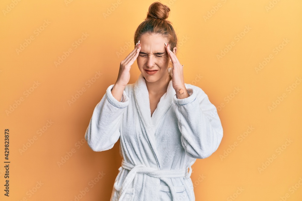 Young blonde woman wearing bathrobe with hand on head for pain in head because stress. suffering migraine. Young blonde woman wearing bathrobe with hand on head for pain in head because stress. suffering migraine.