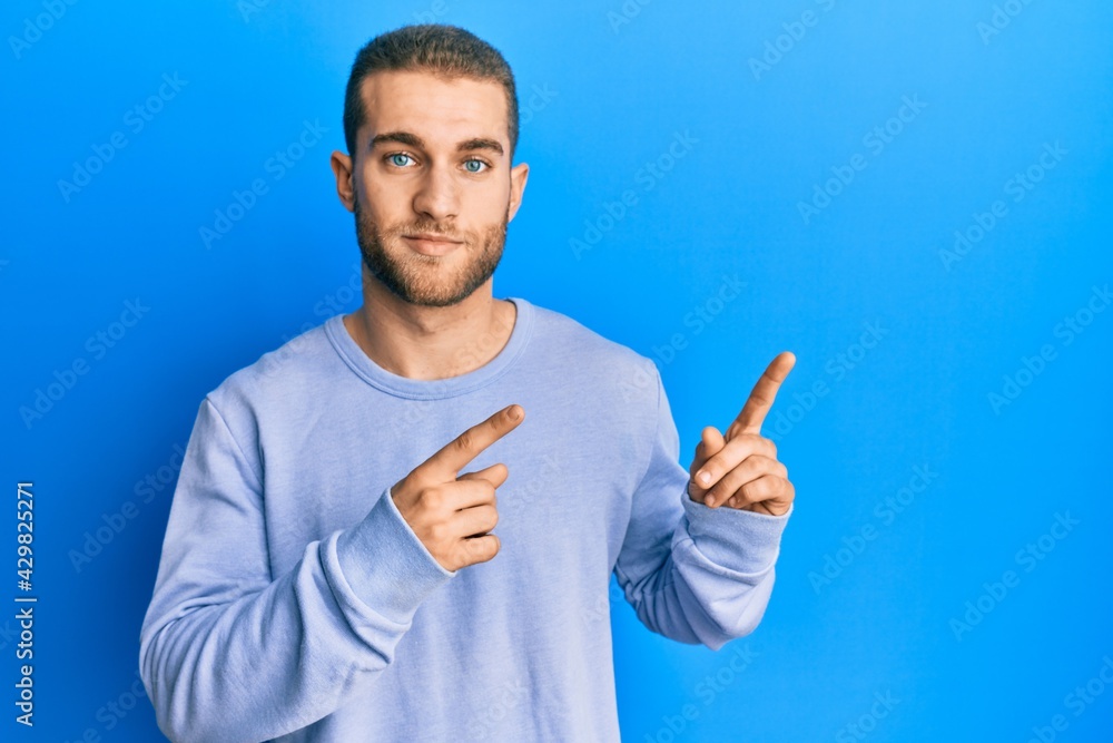 Young caucasian man pointing with fingers to the side relaxed with serious expression on face. simple and natural looking at the camera. Young caucasian man pointing with fingers to the side relaxed with serious expression on face. simple and natural looking at the camera.