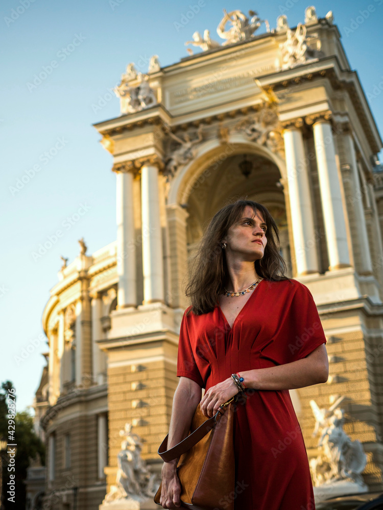 A young woman in a red dress stands near the theater.