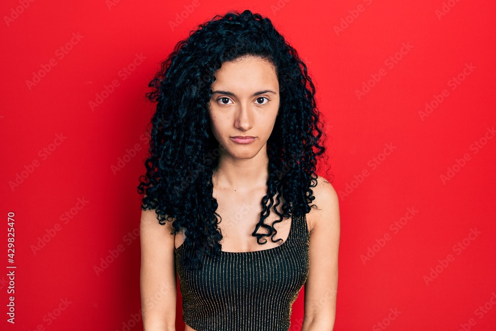 Young hispanic woman with curly hair wearing casual style with sleeveless shirt with serious expression on face. simple and natural looking at the camera. Young hispanic woman with curly hair wearing casual style with sleeveless shirt with serious expression on face. simple and natural looking at the camera.