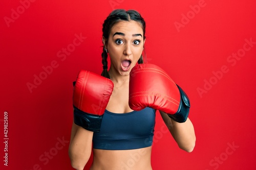 Young brunette girl using boxing gloves afraid and shocked with surprise and amazed expression, fear and excited face. © Krakenimages.com