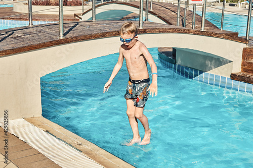 Young boy with bare torsos jumping into swimming pool against sunbeds and palm trees in luxury hotel on sunny day in Greece