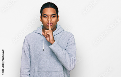 Young handsome hispanic man wearing casual sweatshirt asking to be quiet with finger on lips. silence and secret concept.