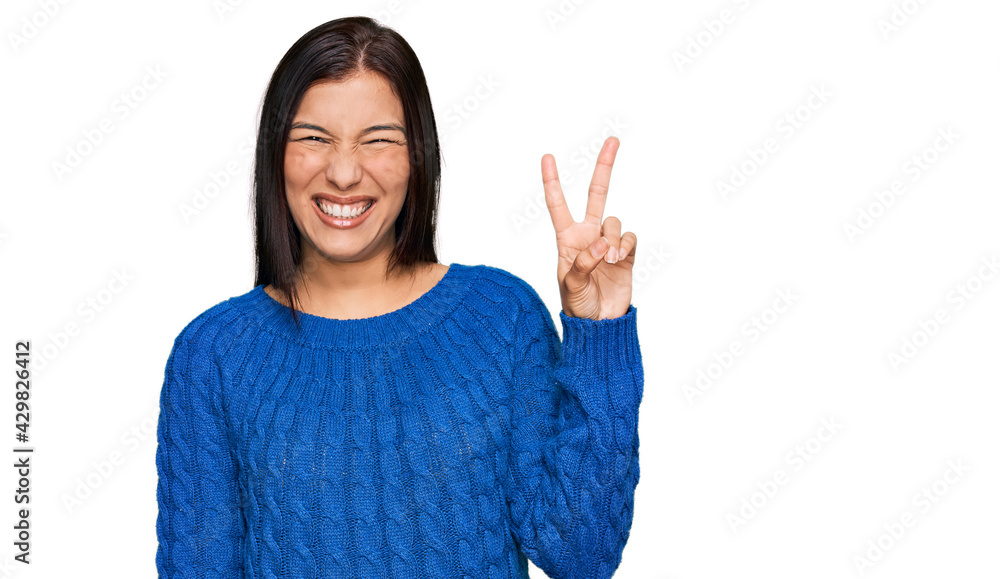 Young hispanic woman wearing casual clothes smiling with happy face winking at the camera doing victory sign with fingers. number two. Young hispanic woman wearing casual clothes smiling with happy face winking at the camera doing victory sign with fingers. number two.