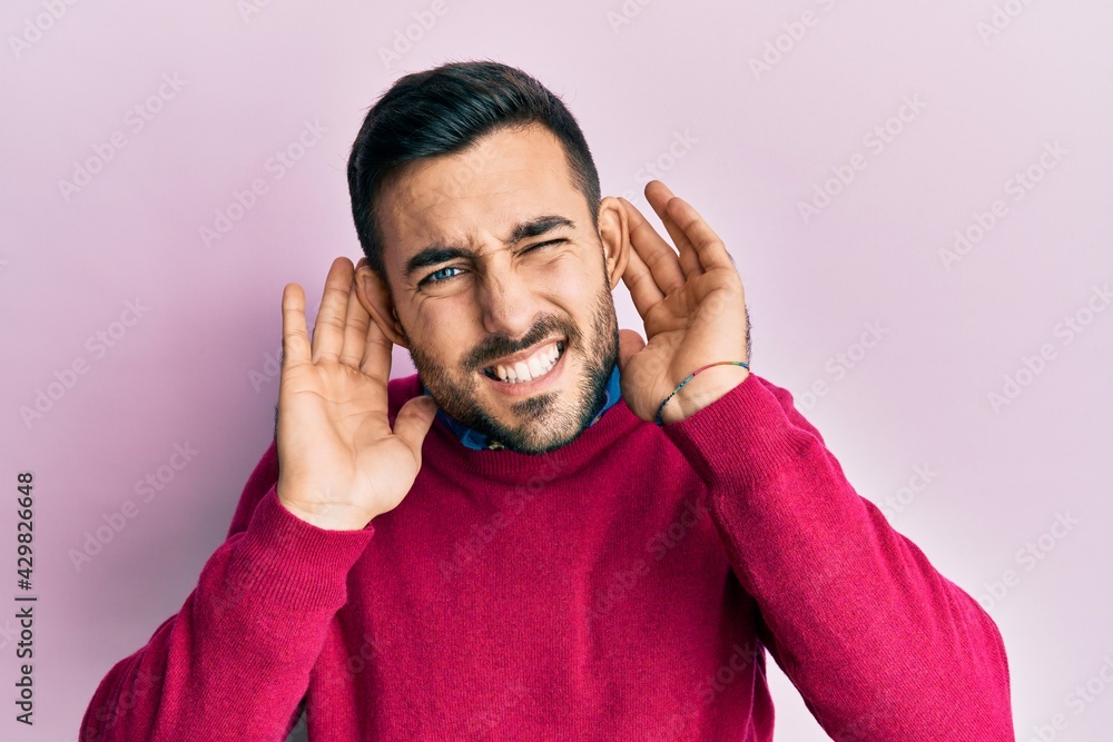 Fototapeta premium Young hispanic man wearing casual clothes trying to hear both hands on ear gesture, curious for gossip. hearing problem, deaf
