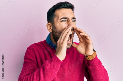 Young hispanic man wearing casual clothes shouting angry out loud with hands over mouth