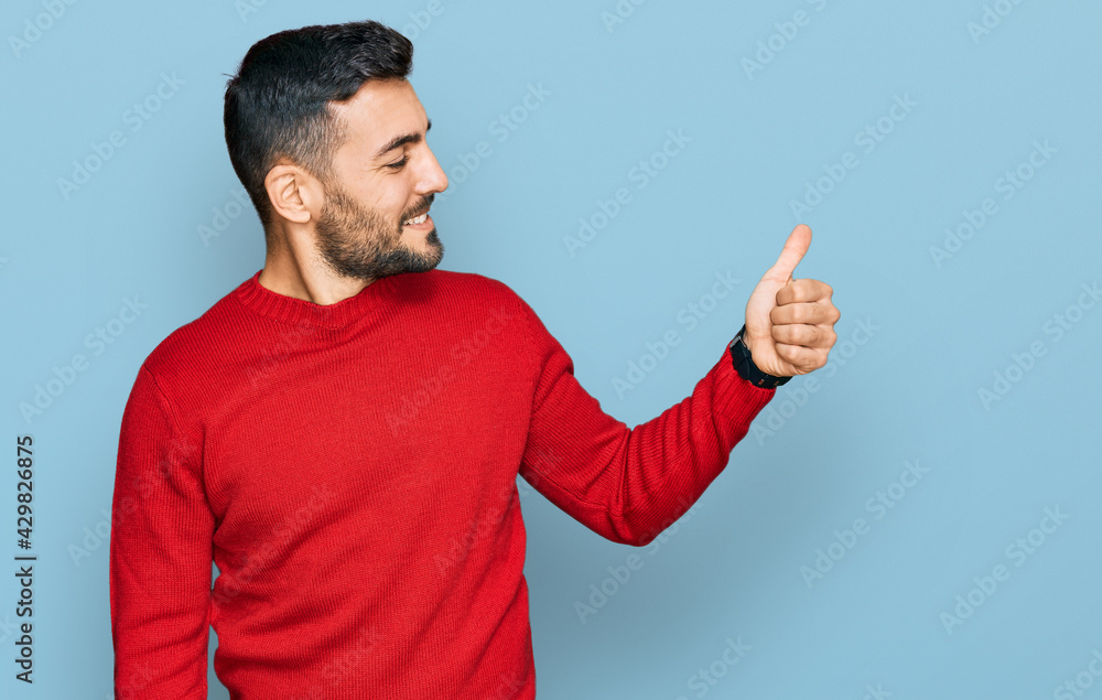 Young hispanic man wearing casual clothes looking proud, smiling doing thumbs up gesture to the side Young hispanic man wearing casual clothes looking proud, smiling doing thumbs up gesture to the side