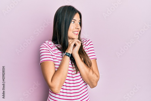 Young brunette woman wearing casual clothes over pink background laughing nervous and excited with hands on chin looking to the side