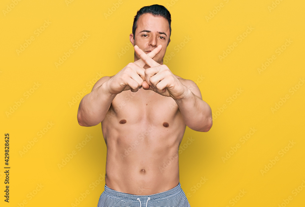 Handsome young man wearing swimwear shirtless rejection expression crossing fingers doing negative sign