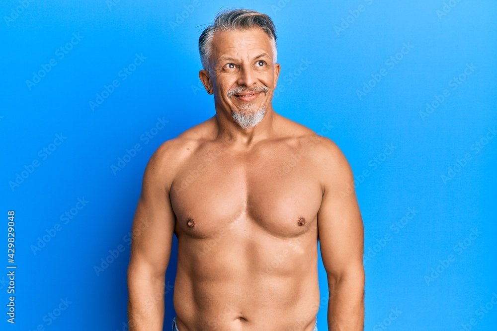 Fototapeta premium Middle age grey-haired man standing shirtless smiling looking to the side and staring away thinking.