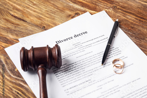 Divorce decree with judge's gavel and rings on wooden background