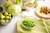 Bowls with green peas and brussels sprouts on light background