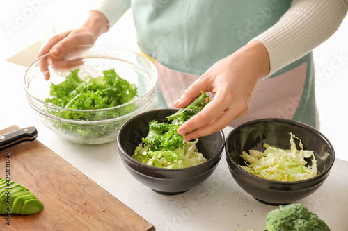 Woman making tasty salad with fresh vegetables on light table