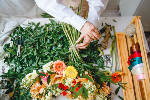 A florist ties a bouquet of fresh flowers with twine on his desk littered with cut leaves. Top view