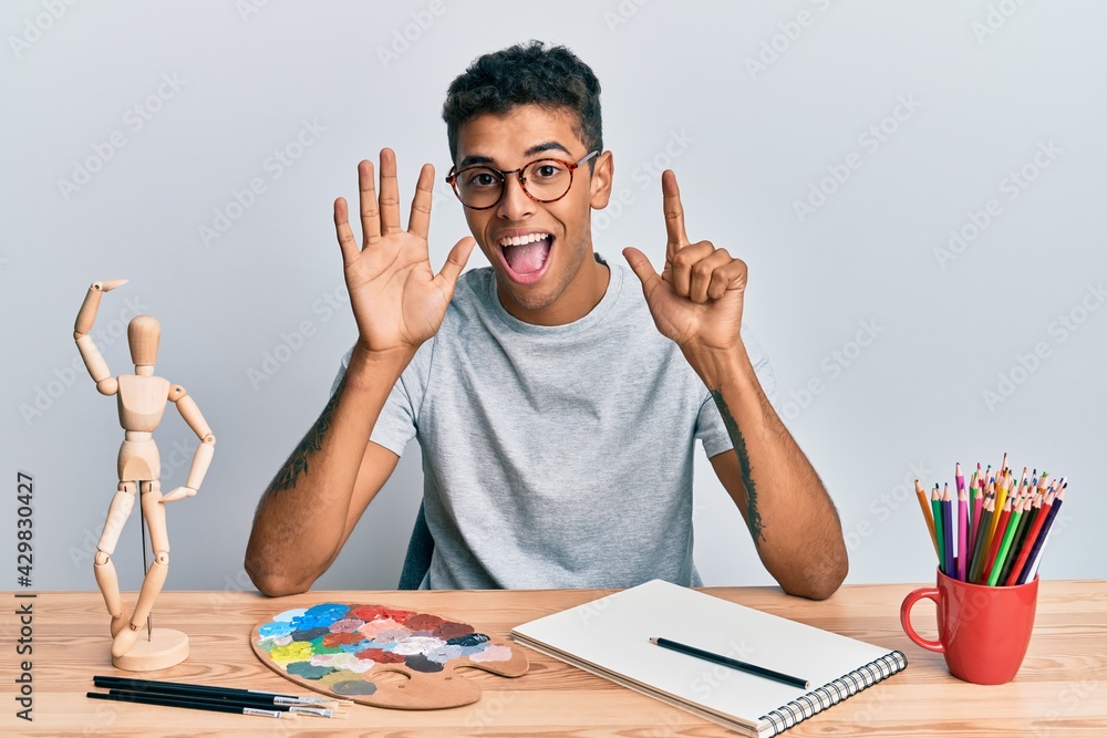 Young handsome african american man painter sitting palette and art manikin showing and pointing up with fingers number seven while smiling confident and happy. Young handsome african american man painter sitting palette and art manikin showing and pointing up with fingers number seven while smiling confident and happy.