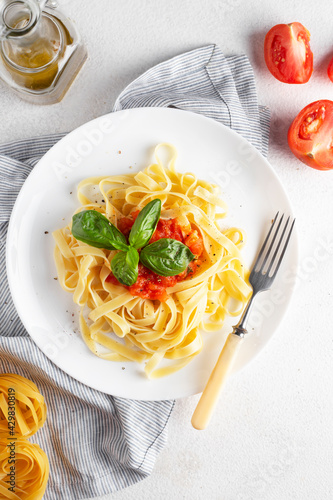 pasta with tomatoes and Basil in a white plate, on a white table, top view