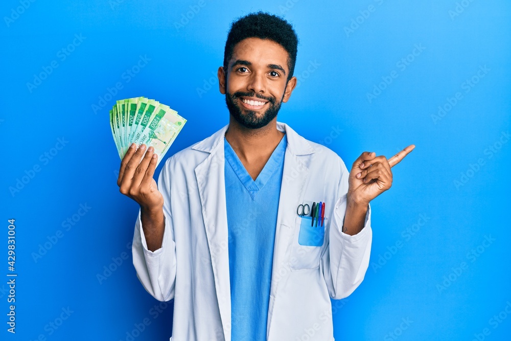Handsome hispanic man with beard wearing medical uniform holding 200 russian ruble smiling happy pointing with hand and finger to the side Handsome hispanic man with beard wearing medical uniform holding 200 russian ruble smiling happy pointing with hand and finger to the side