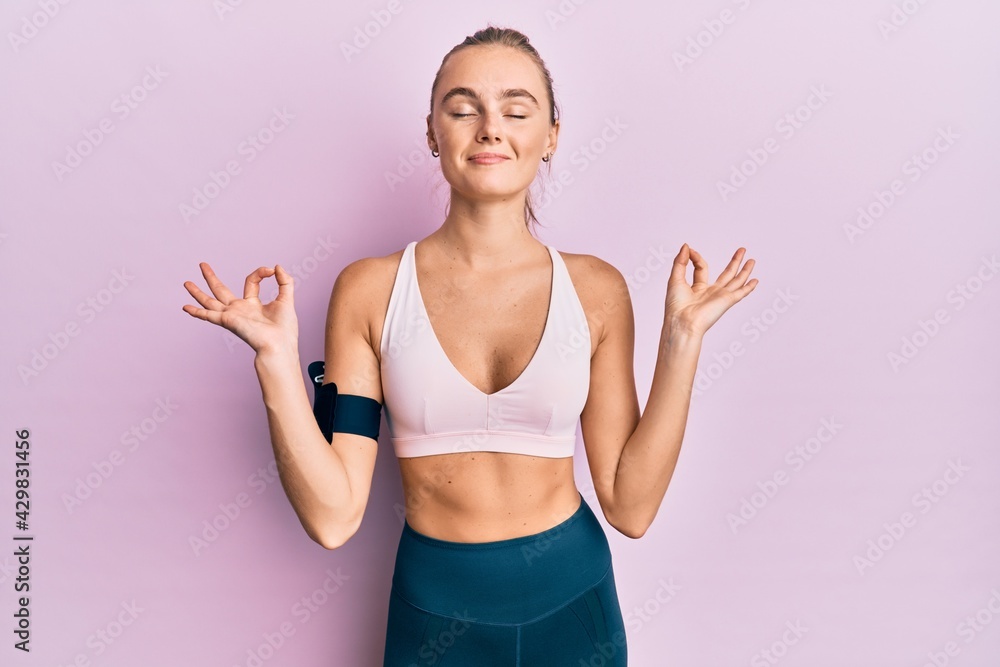 Beautiful blonde woman wearing sportswear and arm band relax and smiling with eyes closed doing meditation gesture with fingers. yoga concept.