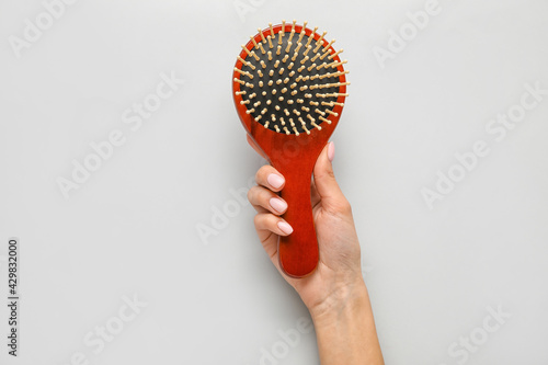 Female hand with wooden hair brush on light background