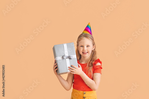 Cute little girl in party hat and with gift on color background