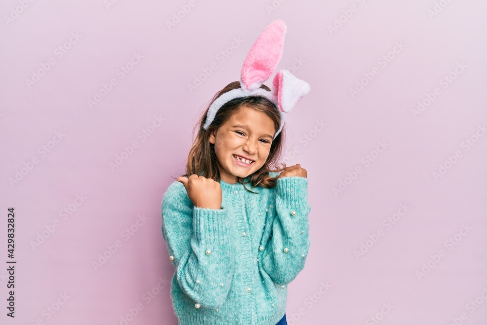 Little beautiful girl wearing cute easter bunny ears very happy and excited doing winner gesture with arms raised, smiling and screaming for success. celebration concept. Little beautiful girl wearing cute easter bunny ears very happy and excited doing winner gesture with arms raised, smiling and screaming for success. celebration concept.