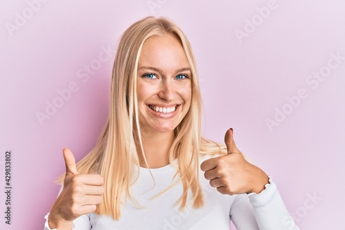 Young blonde girl wearing casual clothes success sign doing positive gesture with hand, thumbs up smiling and happy. cheerful expression and winner gesture.