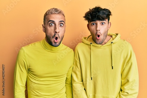 Homosexual gay couple standing together wearing yellow clothes afraid and shocked with surprise expression, fear and excited face.