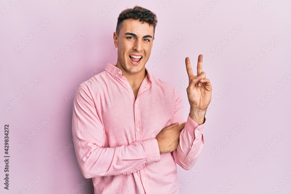 Hispanic young man wearing casual clothes smiling with happy face winking at the camera doing victory sign. number two. Hispanic young man wearing casual clothes smiling with happy face winking at the camera doing victory sign. number two.