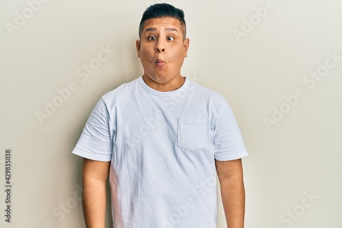 Young latin man wearing casual white t shirt making fish face with lips, crazy and comical gesture. funny expression.