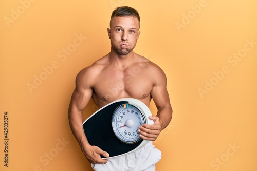 Handsome muscle man holding weight machine to balance weight loss puffing cheeks with funny face. mouth inflated with air  catching air.