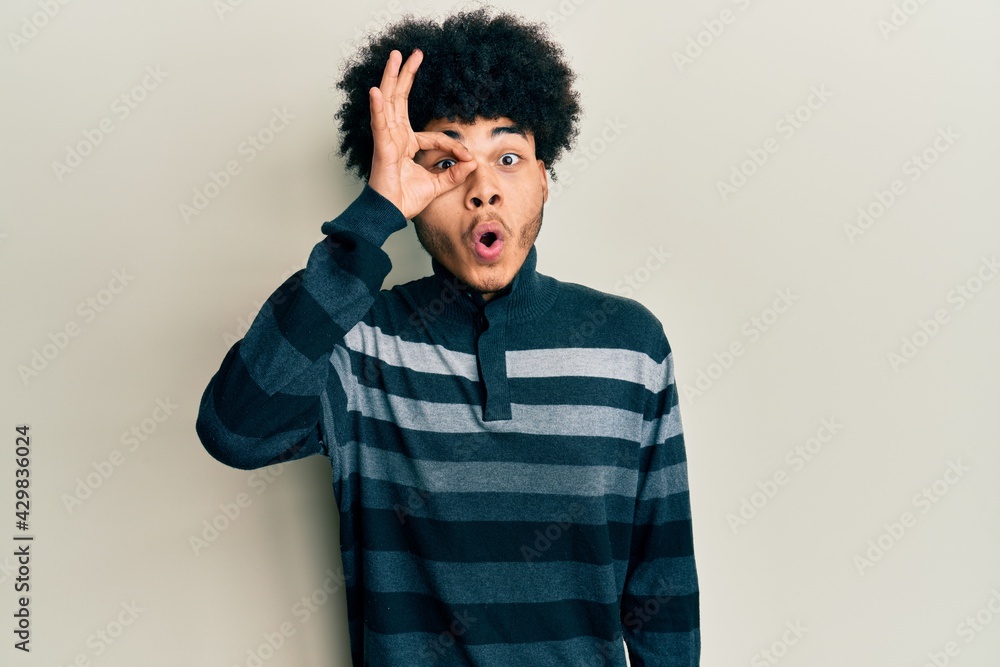 Young african american man with afro hair wearing casual clothes doing ok gesture shocked with surprised face, eye looking through fingers. unbelieving expression. Young african american man with afro hair wearing casual clothes doing ok gesture shocked with surprised face, eye looking through fingers. unbelieving expression.