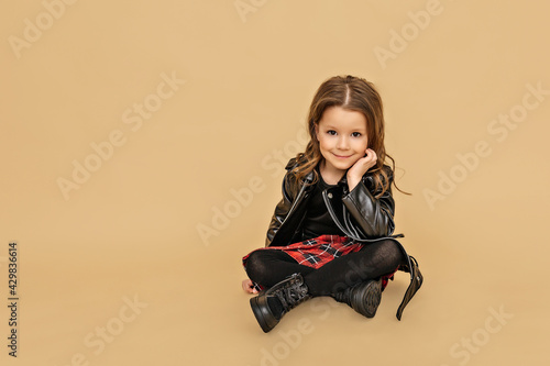 Cute little girl in autumn clothes sits at the beige background.