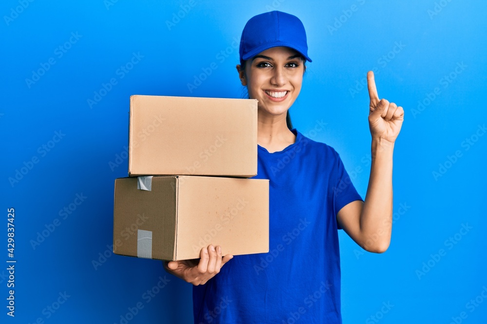 Young hispanic woman holding delivery package smiling with an idea or question pointing finger with happy face, number one Young hispanic woman holding delivery package smiling with an idea or question pointing finger with happy face, number one