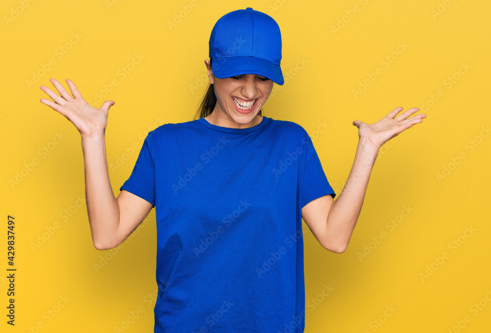 Young hispanic girl wearing delivery courier uniform celebrating mad and crazy for success with arms raised and closed eyes screaming excited. winner concept