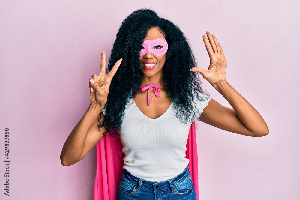 Middle age african american woman wearing super hero costume showing and pointing up with fingers number seven while smiling confident and happy. Middle age african american woman wearing super hero costume showing and pointing up with fingers number seven while smiling confident and happy.
